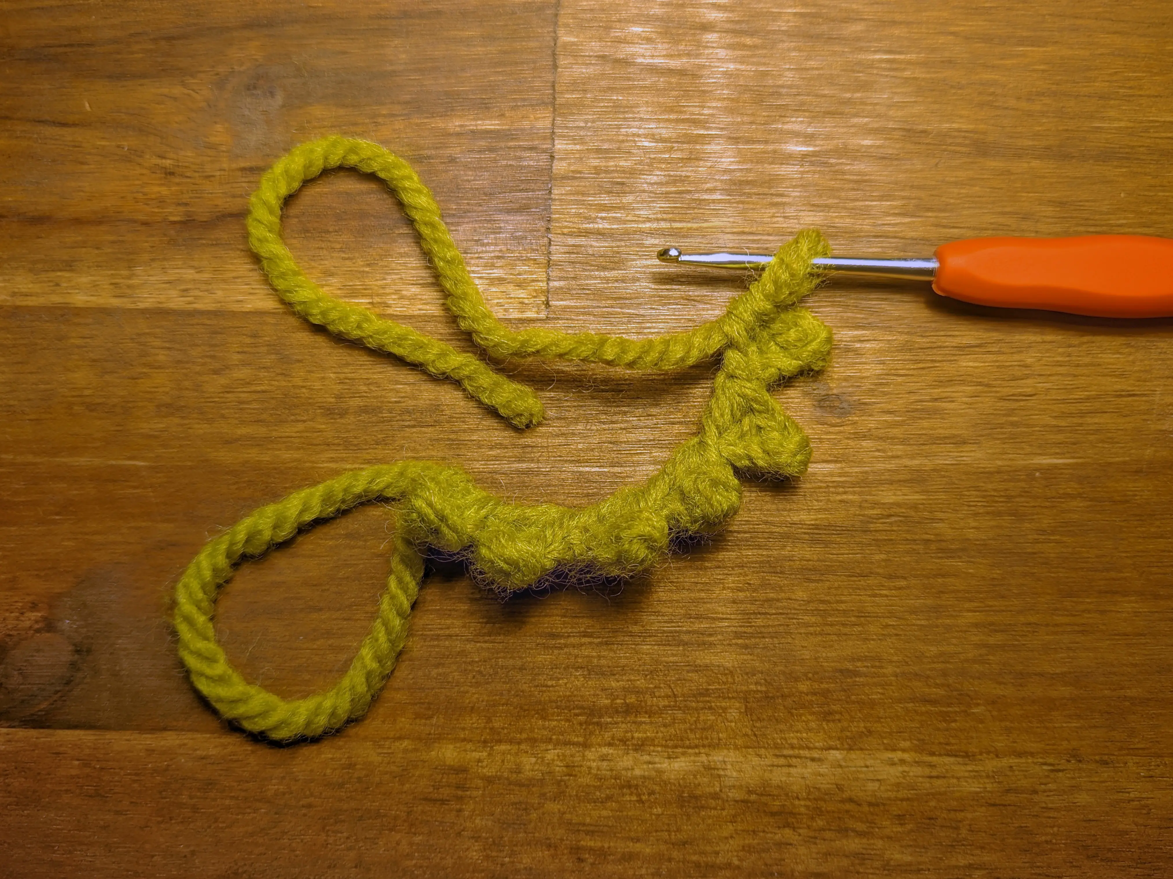 Six connected pointy leaves made from green yarn hanging on a crochet hook
