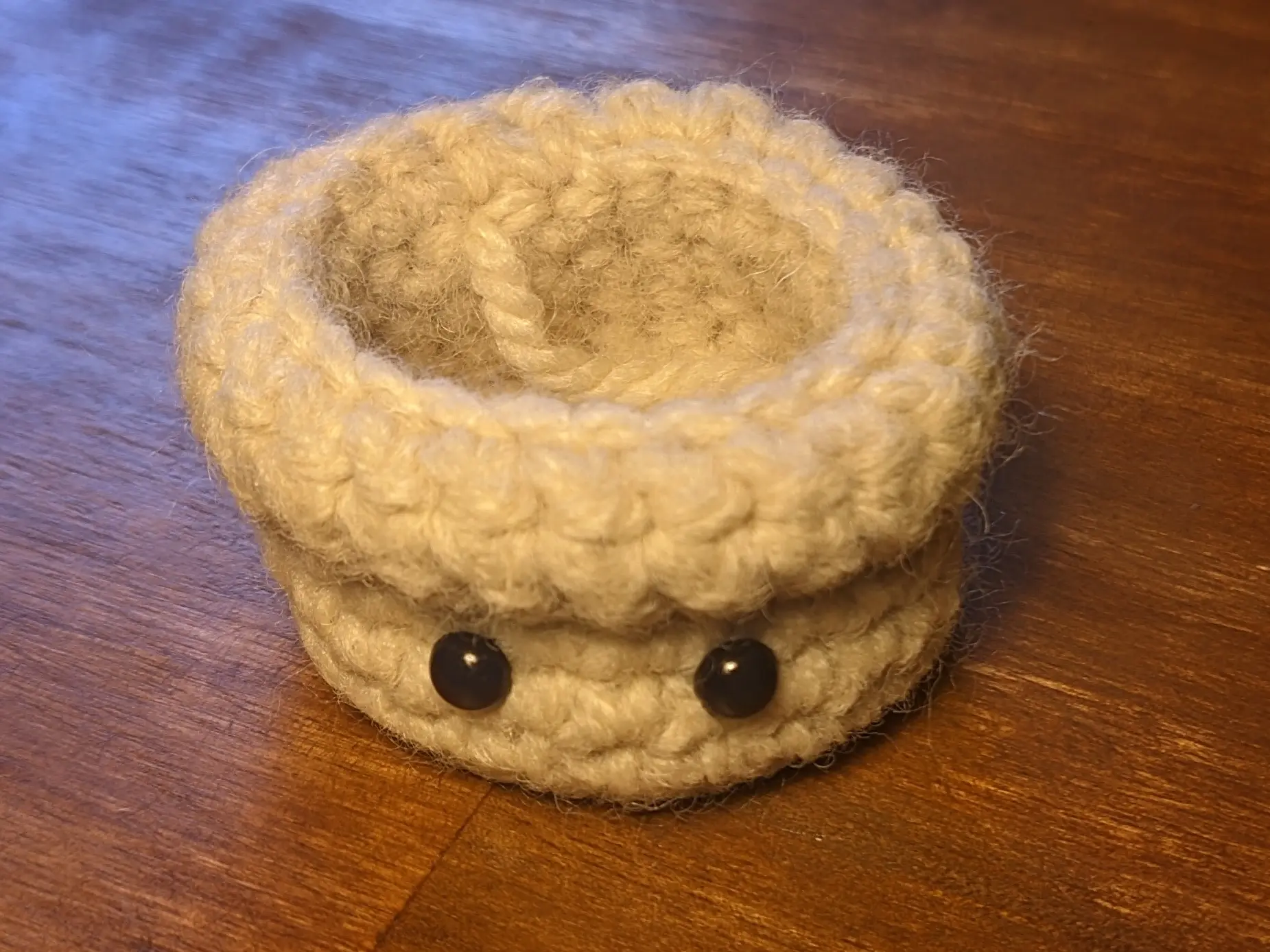 Pot with small black plastic eyes looking at the camera.
The eyes are placed roughly halfway between the bottom and the folded-over overhang.