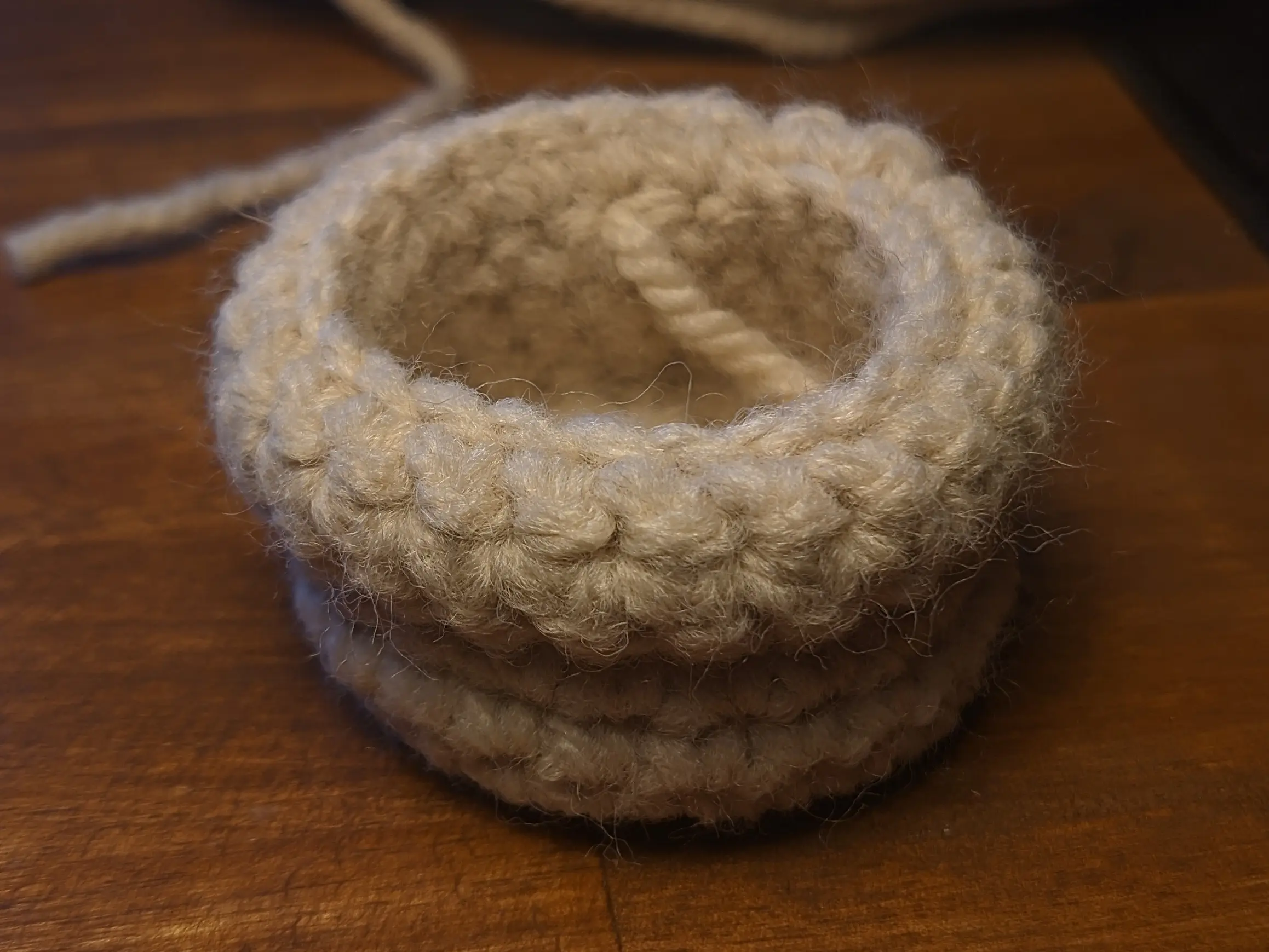 The overhang section has been folded down, with the end of the yarn running inside the cylinder now, entering the inside from below the still-unused inner loops.
The overhang extends about one-third of the pot height downwards.