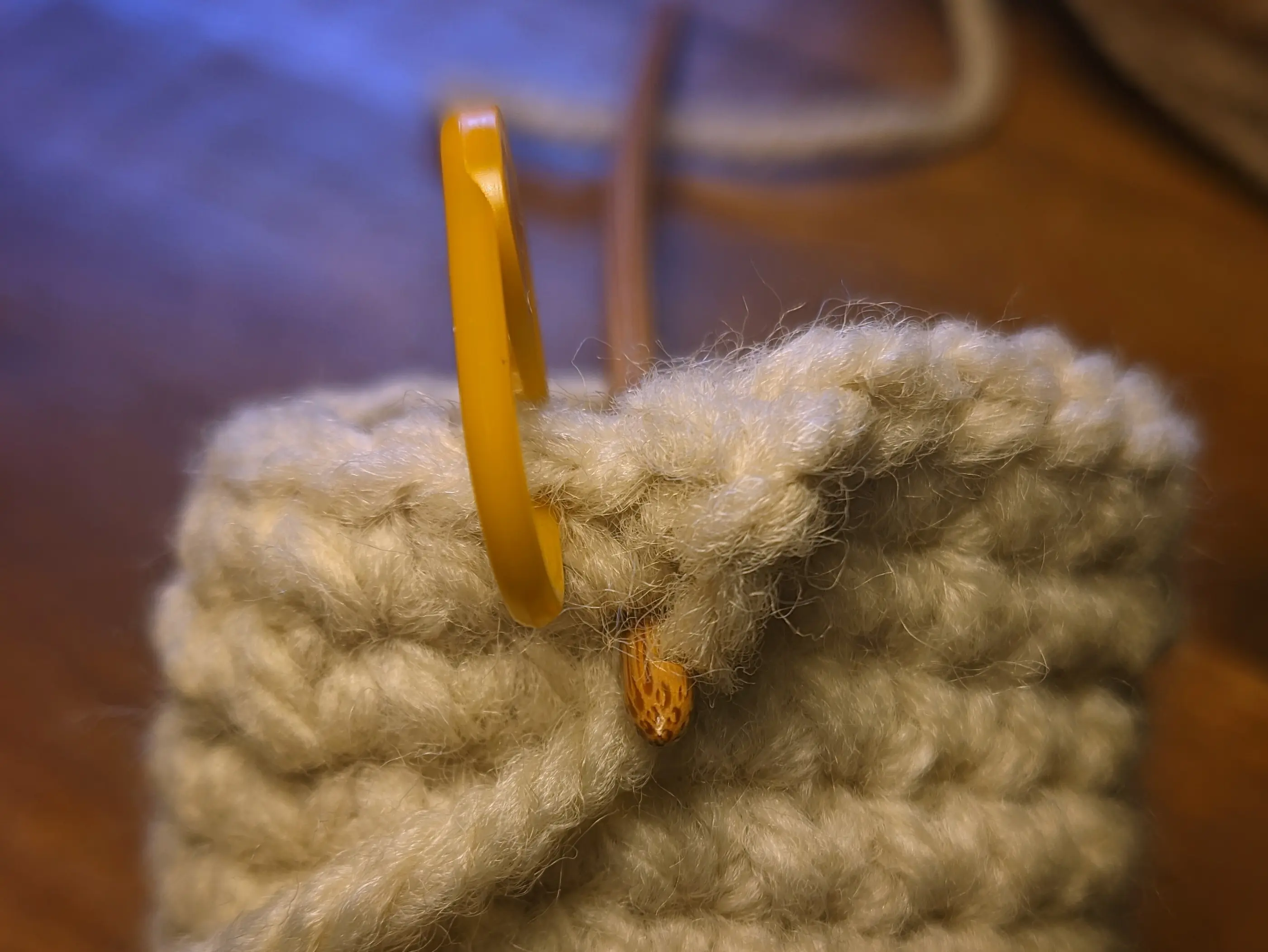 Closeup of the crochet hook being poked from the inside of the cylinder through the stitch below the row of half-loops.
The hook is already catching the end of the yarn.