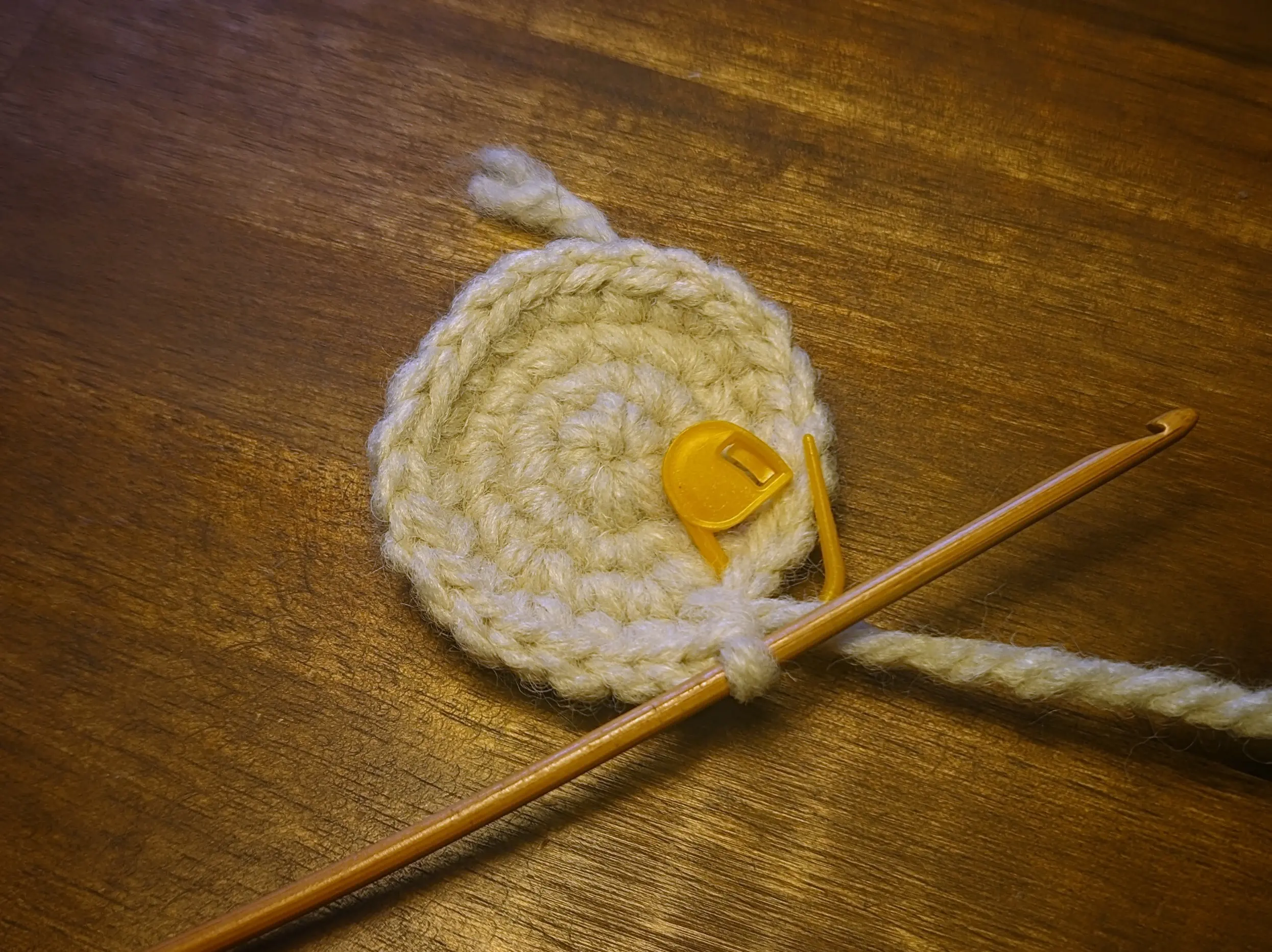 A larger crochet disk with a stitch marker marking the first stitch of the next round.
There are four rounds in total, one of which is from the magic circle.