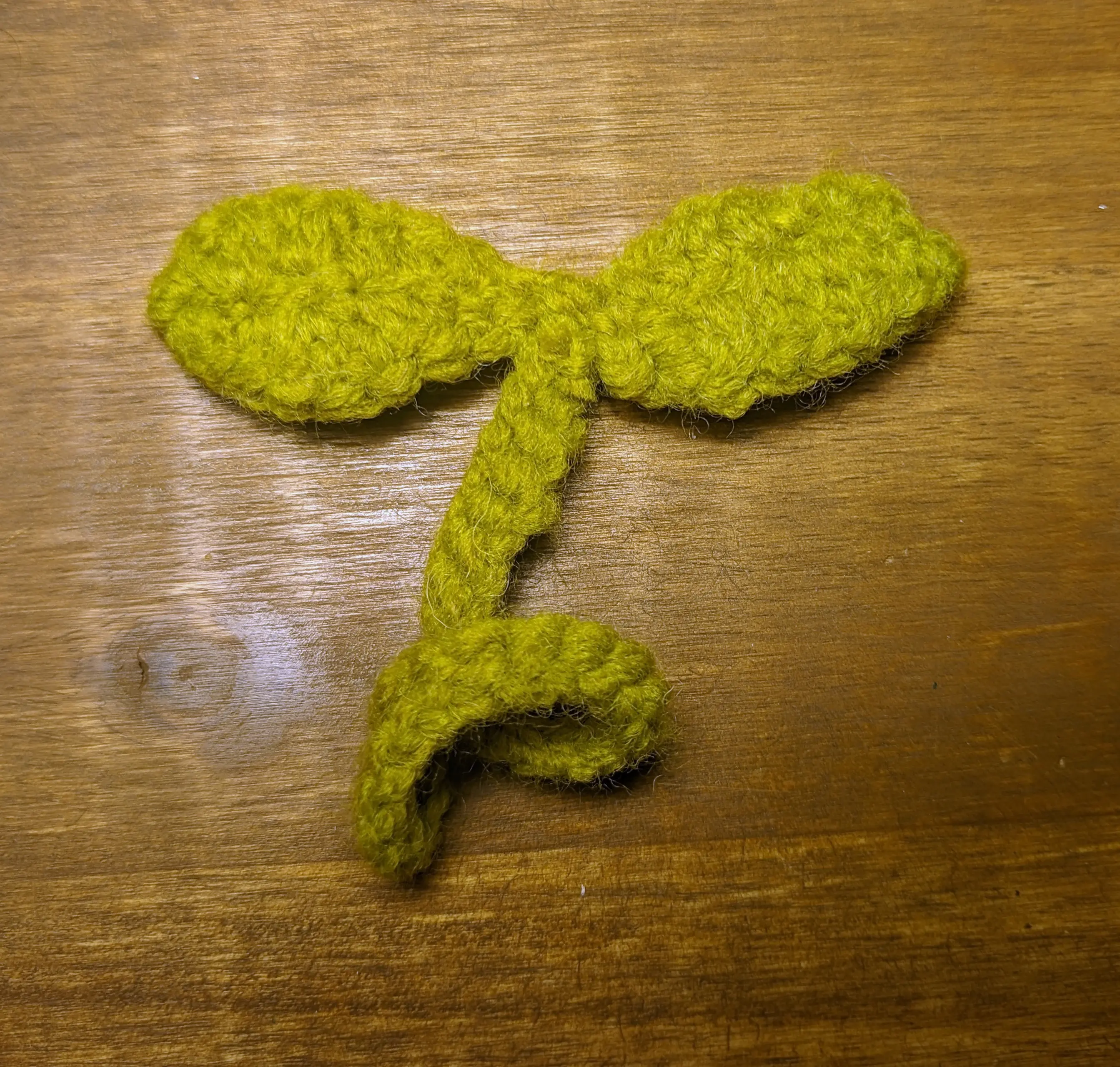 The same stem-like crochet chain, from the bottom with both leaves sewn to it. One on the left, the other on the right side. Both leaves are also facing down.
