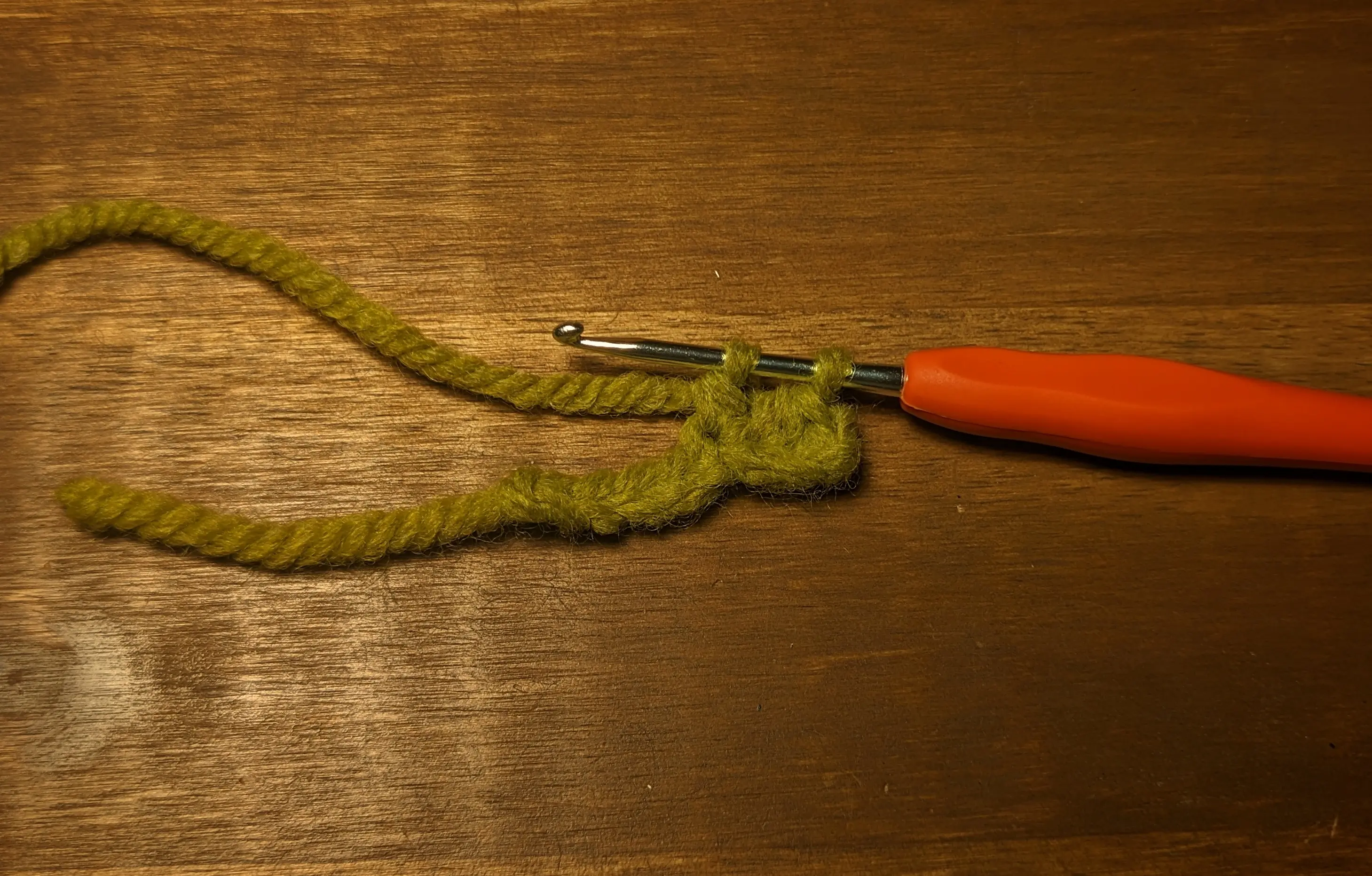 Crochet chain with some stitches on one side. The crochet hook has two active loops on it.