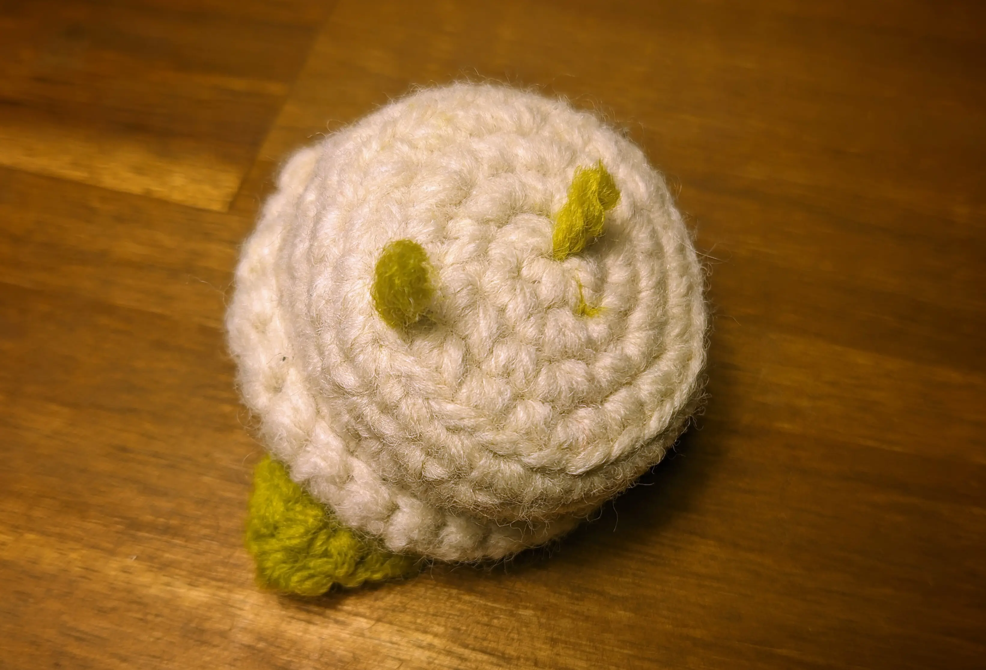 Crochet flowerpot flipped upside down. Two green yarn ends are coming out of the bottom loops.