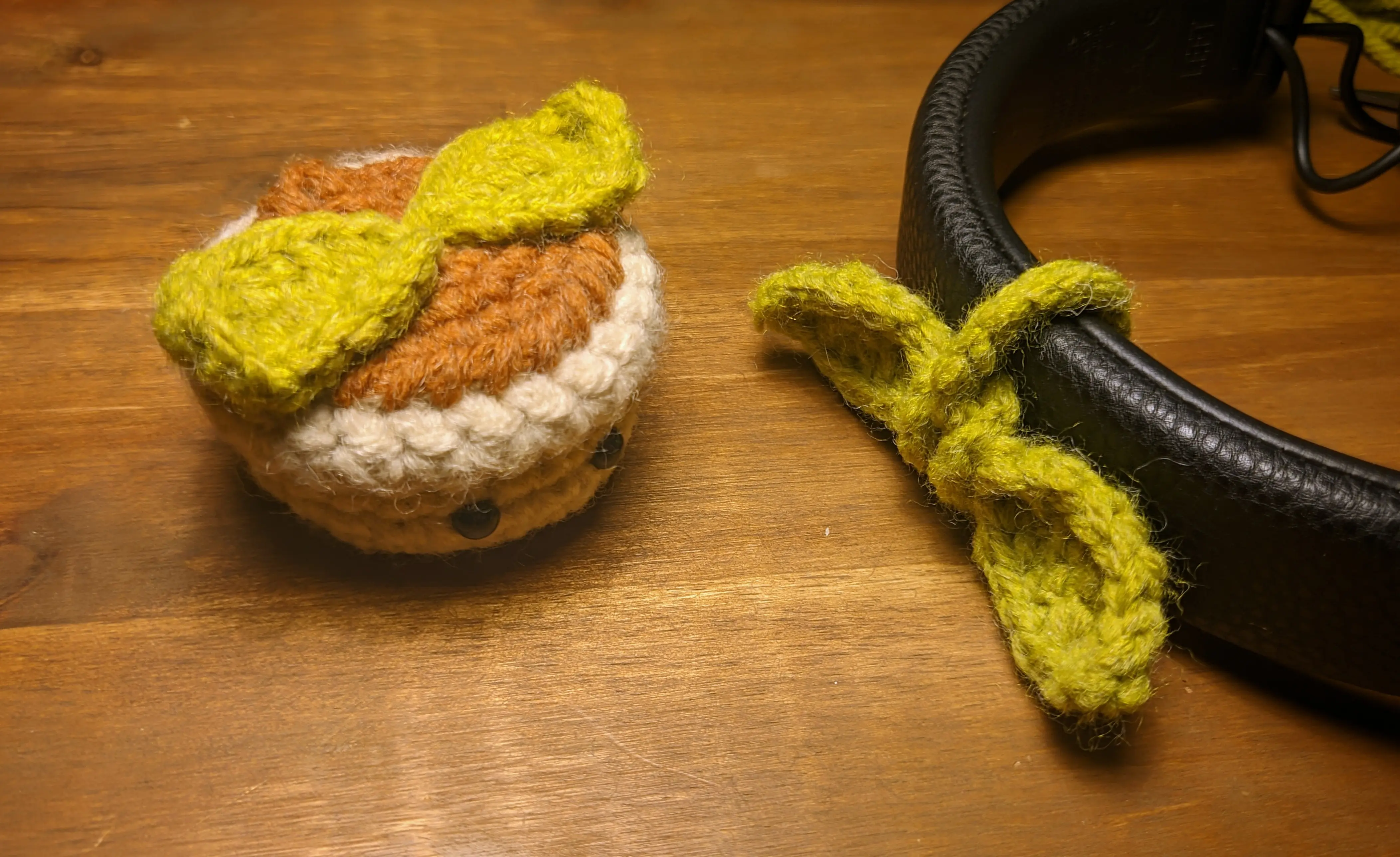 The finished flowerpot with two oval leaves on top, placed next to a pair of headphones with the leaf loop wrapped around it, sitting on a wooden desk.
