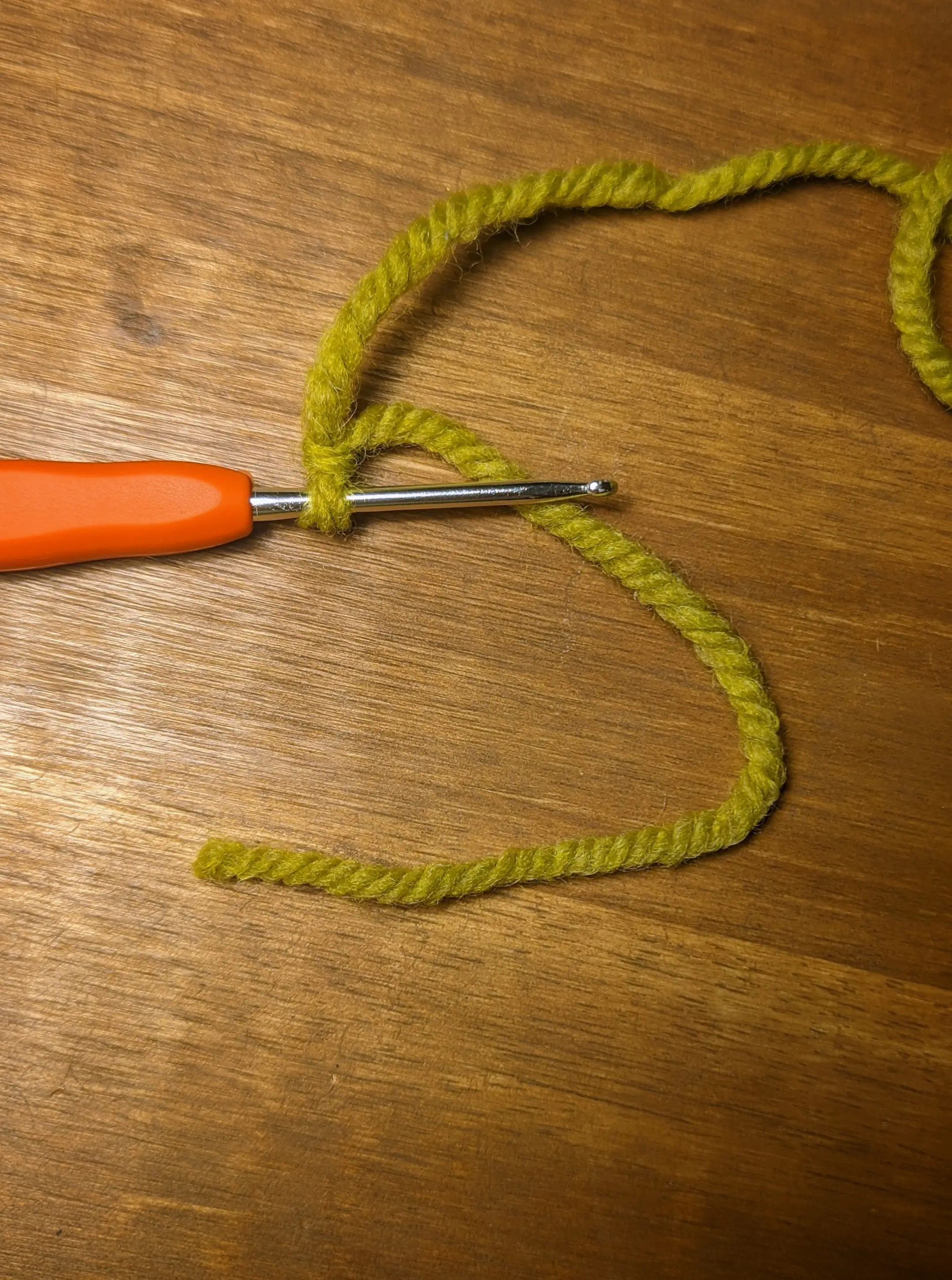 Green yarn tied in a loop around the crochet hook. The active yarn is running off-screen, but the start section has about 7 cm of excess material.