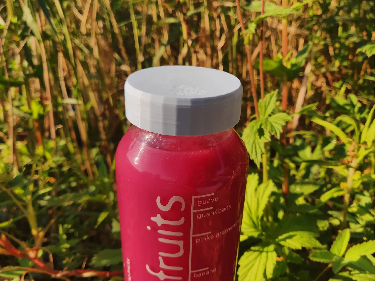 True fruits bottle with a blue 3D-printed lid screwed on top. The bottle is filled with a pink smoothie.
