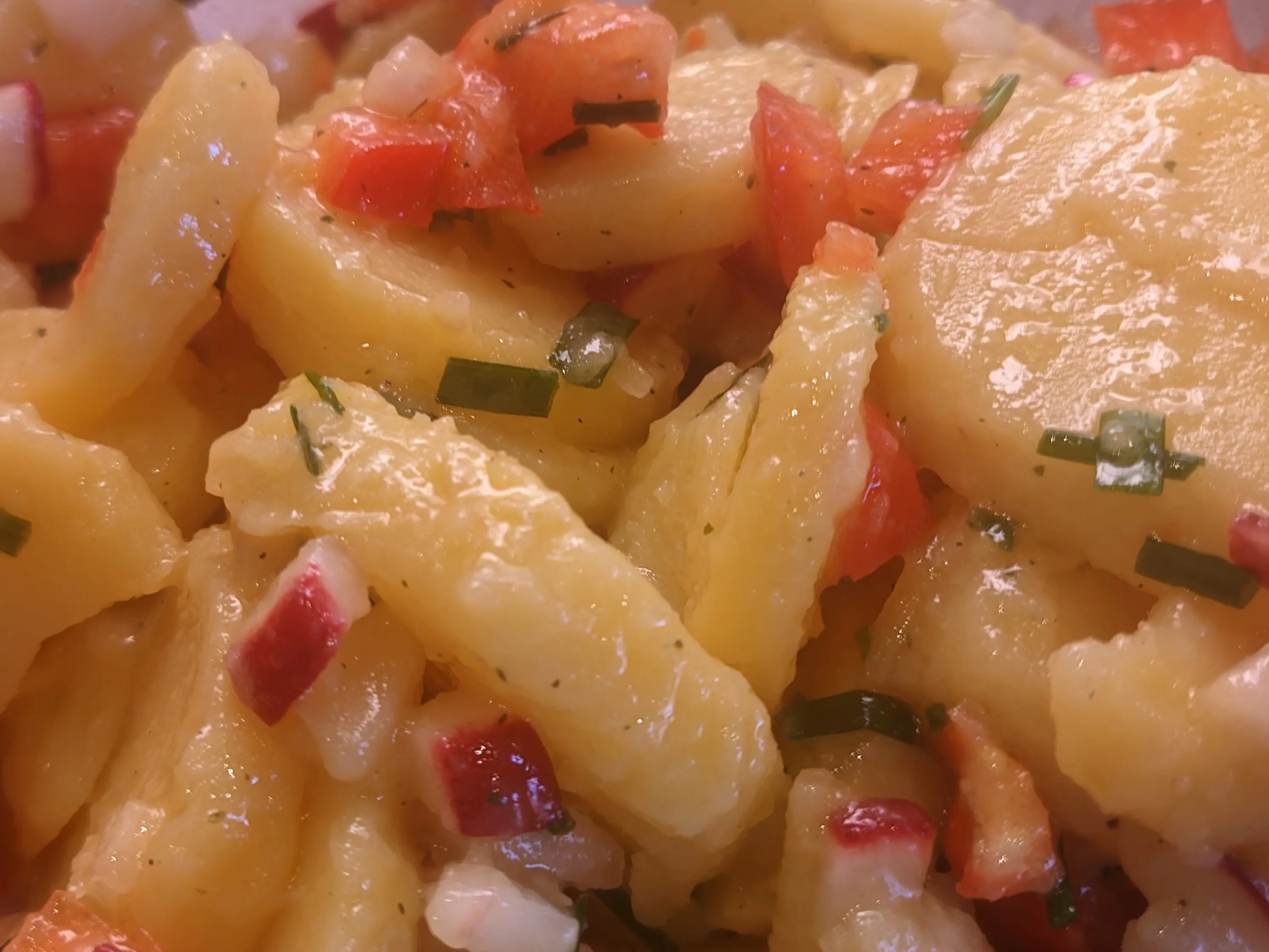Closeup of the potato salad.
The potato slices are mixed with the cut bell peppers, radishes and some green chives between.
The sauces have formed a fairly thick coating over the potatoes.